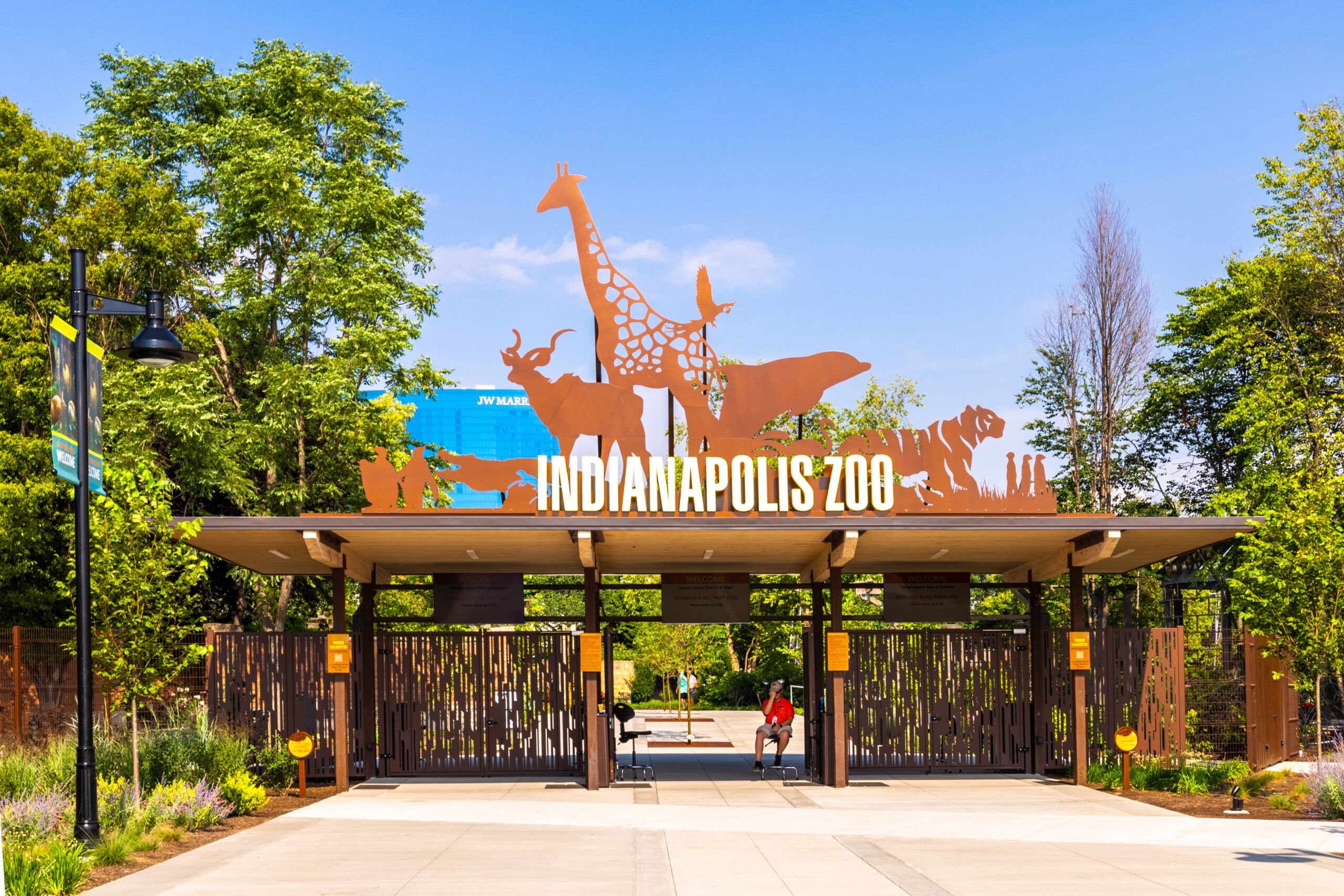 The entrance to the Indianapolis Zoo welcomes visitors with animal silhouettes set against lush greenery and a bright blue sky.